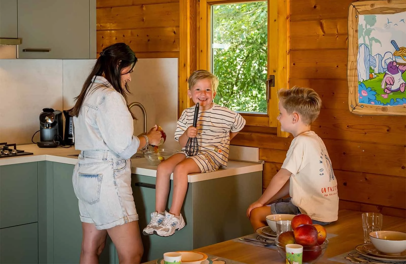 Molletjes Boshut keuken in de Tovertuin, kind zit op het aanrecht voor het raam, vrouw voor het aanrecht en kind bij de tafel.